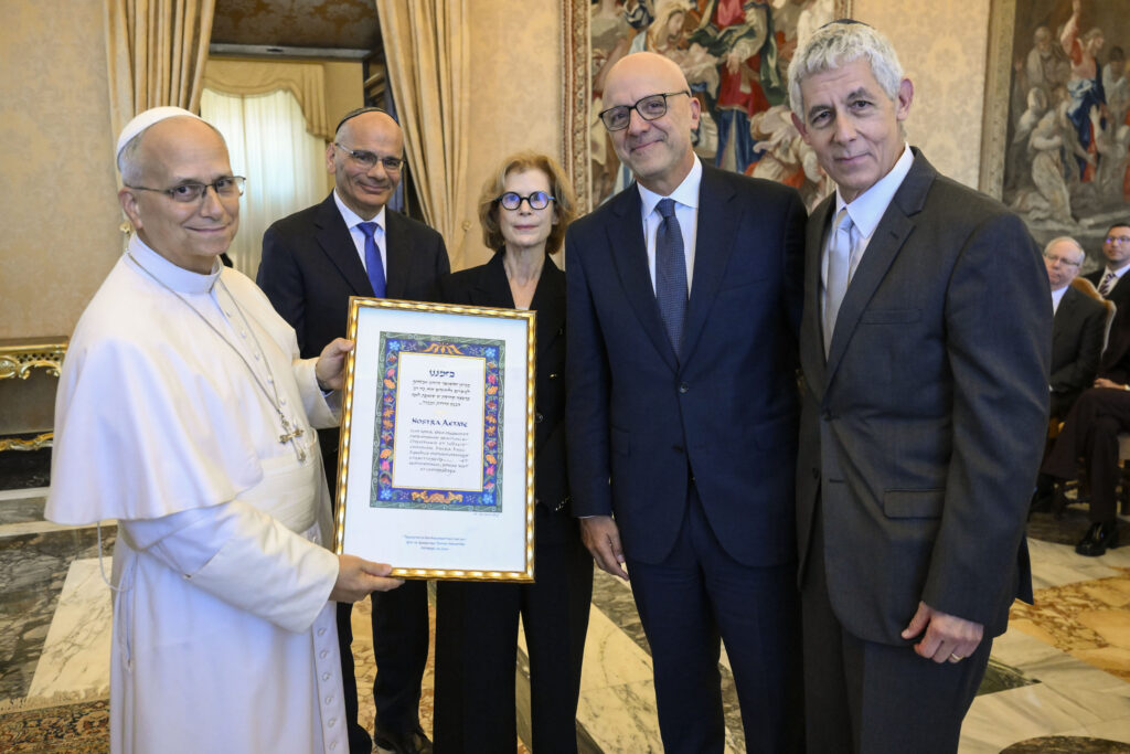 Pope Leo XIV holds a framed copy of a paragraph of “Nostra Aetate,” the Second Vatican Council’s Declaration on the Relation of the Church with Non-Christian Religions, in Latin and Hebrew, as he poses with members of the American Jewish Committee in the Apostolic Palace of the Vatican on Oct. 22, 2026. | Credit: Vatican Media