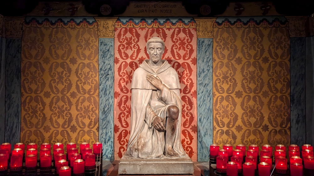 Candles surround a statue of St. Peregrine at a prayer room in Sierra Chapel, Mission San Juan Capistrano, California, on May 4, 2025. | Credit: Tom Windeknecht/Shutterstock
